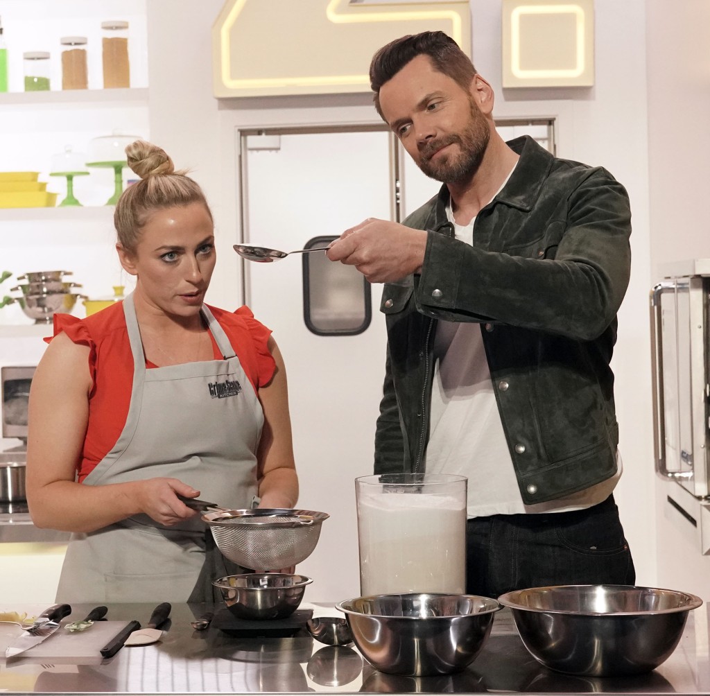 Contestant Natasha with host Joel McHale measure ingredients together in a kitchen in "Crime Scene Kitchen." 