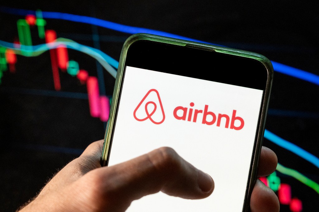 CHINA - 2021/12/09: In this photo illustration the American online marketplace and hospitality service Airbnb logo seen displayed on a smartphone with an economic stock exchange index graph in the background. (Photo Illustration by Budrul Chukrut/SOPA Images/LightRocket via Getty Images)